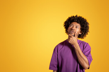 Fototapeta na wymiar Serious pensive black adult curly man in purple t-shirt, thinks, look at copy space