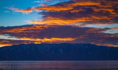 Scenic cloudscape on a blue sky at sunset with silhouettes of hills and a lake under
