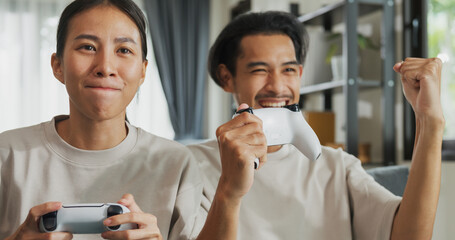 Close-up Young Asian couple sit on couch hold joystick play video game spend time together have fun...