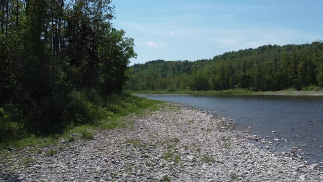 Drone footage of the rocky shore of the calm Matane river on a sunny day