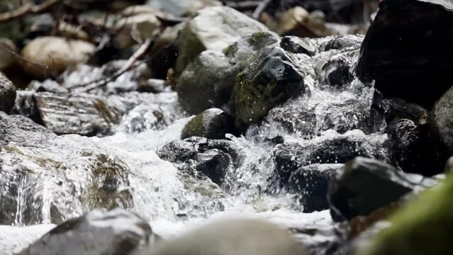 Closeup of a small waterfall stream on rocks under the sunlight in forest.