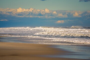 Scenic shot of foamy ocean waves hitting the shore with the illuminated clouds in the sky