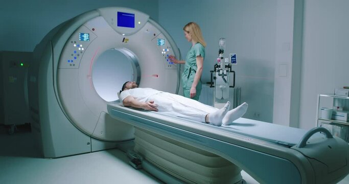 Male patient lies at TC scanner bed. Man goes out of MRI capsule. Female doctor dressed up in uniform have talk with patient. Medical worker smiling and pushes buttons of MRI capsule.