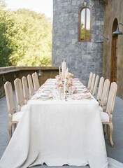 Long wedding reception table with white cloth cover with trees in the background outdoors