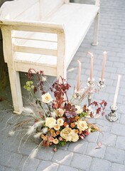Garden roses bouquet and chandelier with candles next to an empty wooden long seat