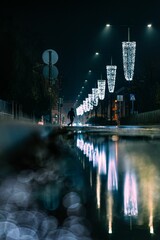 lights strung over an urban street reflecting in the water at night