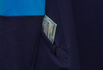 Hundred-dollar bills are visible from the pocket of a blue sports jacket.