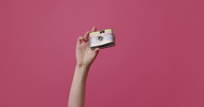 A woman's hand takes photos with a retro camera and shows the like sign on an isolated pink background.