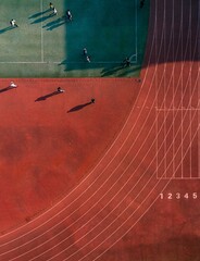 Aerial top view of a brown running track and a green court with people on a sunny day