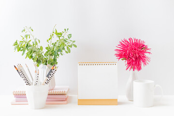 Mockup white desk calendar and red flowers in a vase on a light background. Spiral calendar for...