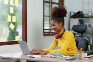 Beautiful young black woman working with laptop computer at home. Young african american female curly hair working on laptop and take note at home.