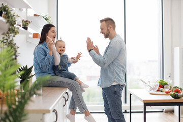 Beautiful brunette woman sitting on countertop with baby on laps while handsome man standing in...
