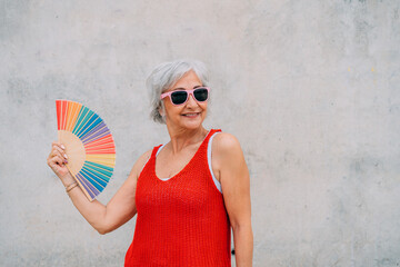 Cheerful elderly woman using rainbow hand fan on street