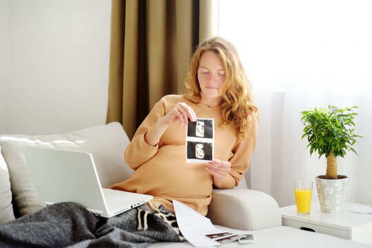 Pregnant caucasian woman resting at home. A young expectant mother reads a doctor's report and looks at ultrasound pictures of her baby.