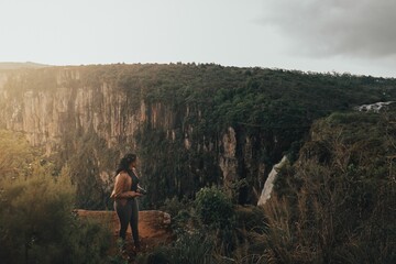 Young black woman taking photos outdoor with landscape green cliffs at sunset