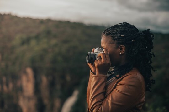 Young black woman taking photos outdoor with green cliffs at sunset