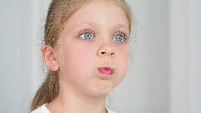 The girl puffed out her cheeks. Facial gymnastics for correct speech. Warming up the muscles of the mouth. Speech therapist exercise.