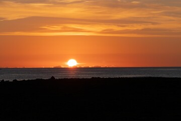 Fototapeta na wymiar Glowing sun in the orange sunset sky going down behind a tranquil seascape