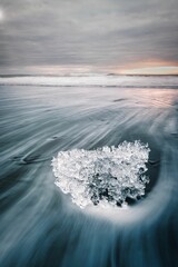 Vertical long exposure of a piece of patterned ice looking like a diamond on a beach in Iceland