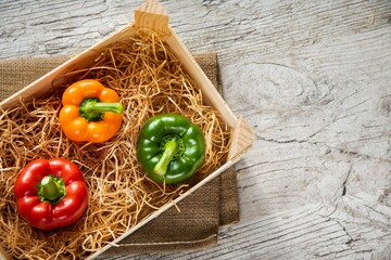 Colorful bell peppers on box on the wooden table, flat lay