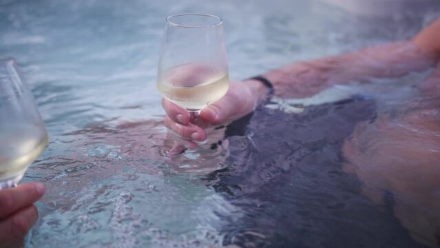 Slow motion view of a couple toasting with glasses of white wine in a jacuzzi