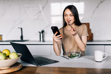 Attractive woman eating salads and using mobile phone. Diet and healthy food concept.
