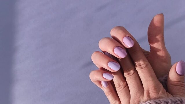 Hands with purple manicure on a monotone in the rays of the sun