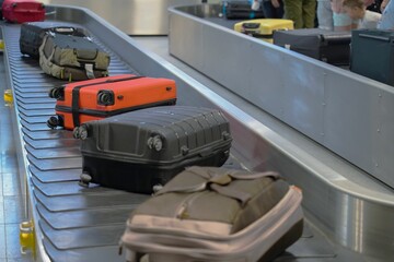 Suitcases on a baggage carousel at an airport with waiting guests in the background