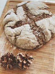 Top view of a homemade baked peasant bread with dried pine cones on a wooden board
