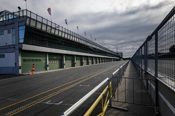 Motor racing of asphalt road by a building with flags and metal fence under cloudy sky