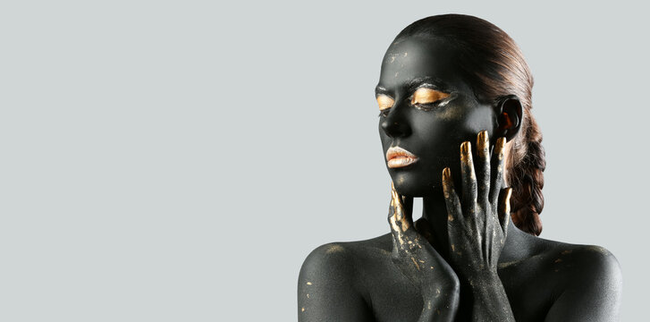 Beautiful woman with black and golden paint on her body against grey background with space for text