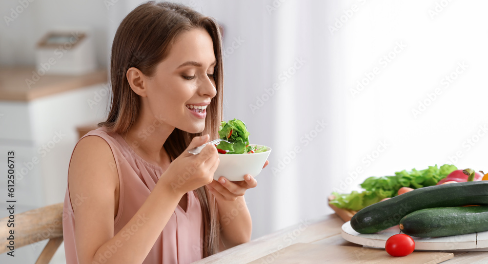 Wall mural Young woman eating vegetable salad in kitchen