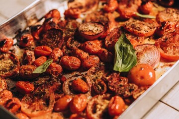Stainless steel pan with red tomatoes, fresh basil, onions and seasonings