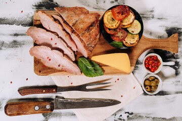 High angle of the sliced ham meat with other ingredients and a knife put on the kitchen marble table