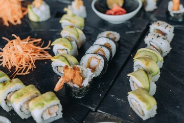 High-angle of different types of sushi rolls put on the black desk on blurred background