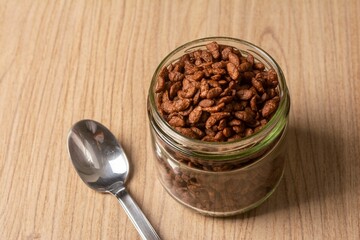 Top view of a jar with candied almonds and a spoon on a wooden table