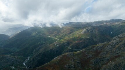 Aerial shot of a highway passing along the green slope of the mountain range under the cloudy sky