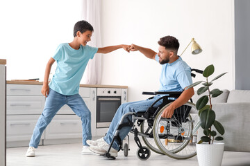 Fototapeta premium Little boy and his father in wheelchair bumping fists at home