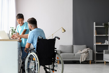 Little boy and his father in wheelchair using laptop at home