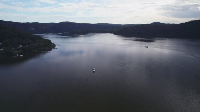 Aerial shot over a boat driving in Hawkesbury River with green hills with sunset sky in Australia