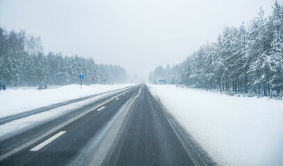 Snowy road through snowy trees on a gloomy day, blank and foggy sky background