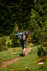Back shot of an adult man walking on a hiking trail in the woods holding his bike on his back