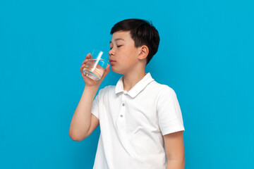 asian boy in white t-shirt drinks clean transparent water on blue background, korean child maintains water balance