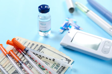 Syringes with money, glucometer and insulin on blue background, closeup. Expensive medicine concept