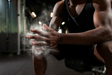 sporty african american man trains in dark gym and rubs his hands with magnesia, young guy makes...