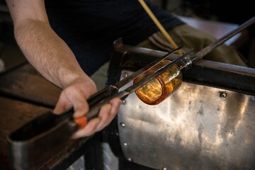 Male glass blower holding orange glass mold with high fire for shaping