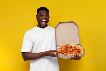 happy african american man in white t-shirt holds box of pizza and rejoices on yellow isolated background
