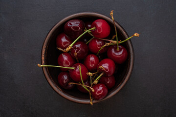 Top view of ripe cherries in a ceramic bowl on a black table.  Berry dessert. Red and black. Juicy berries. Red products. Rural scene. Vegetarian food.