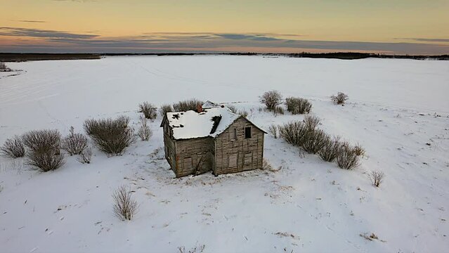 Aerial video of a small abandoned house in the field covered with snow during sunset