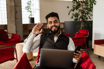 Young indian man in suit using laptop and cellphone at office lobby